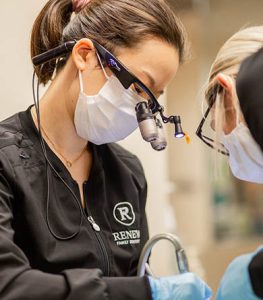 Dentist at Renew Family Dentistry in Frisco, TX, using magnifying glasses and a mask during a dental procedure, emphasizing personalized care for dental implant consultations.