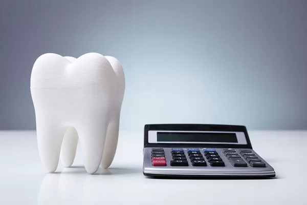 White tooth model next to a calculator, symbolizing dental treatment costs and pricing transparency at Renew Family Dentistry.