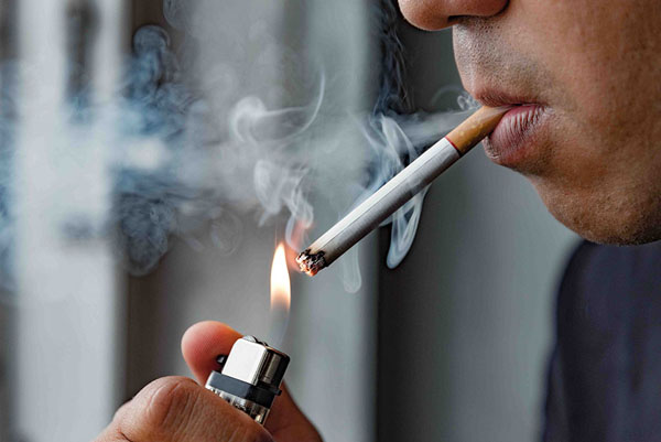 Man lighting a cigarette, smoke rising, illustrating risks associated with nicotine use and its effects on gum health.