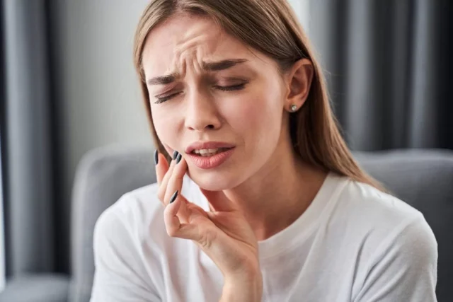 Woman experiencing jaw pain and discomfort, indicating potential bite misalignment after wisdom tooth removal, emphasizing post-operative dental concerns.